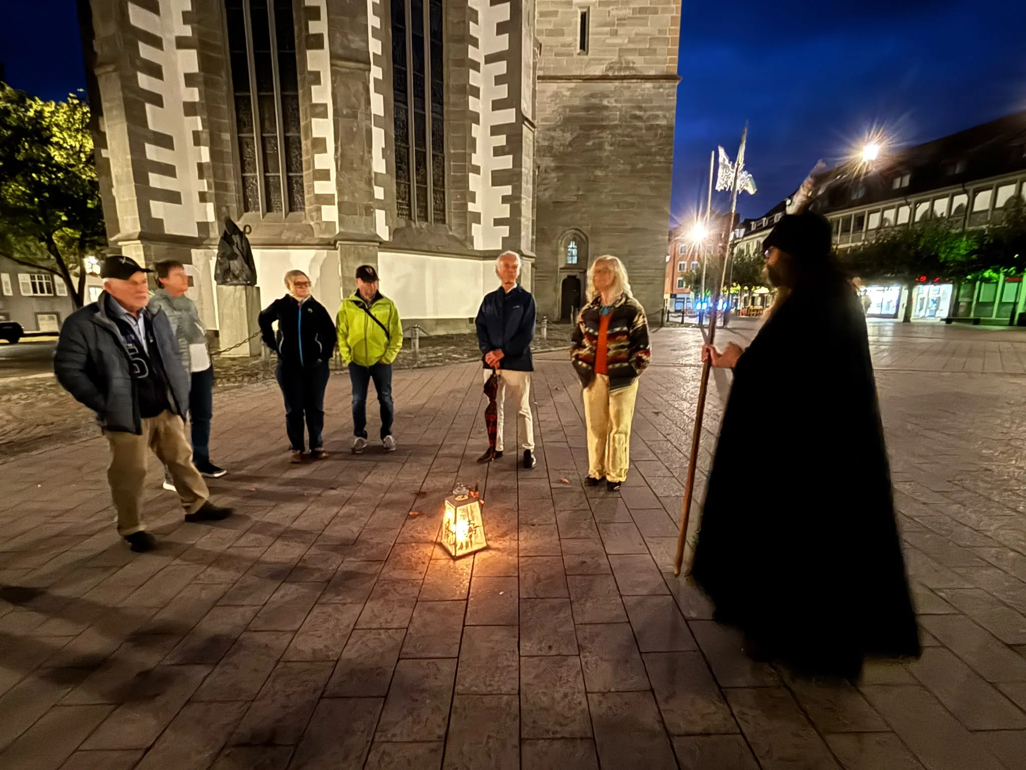 Teilnehmende der Führung mit dem Nachtwächter und seiner Laterne vor dem abendlich beleuchteten Münster